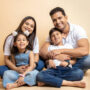 Happy young indian parents and kids wearing casual cloths sitting together on floor isolated over beige studio background. Asian Family bonding.